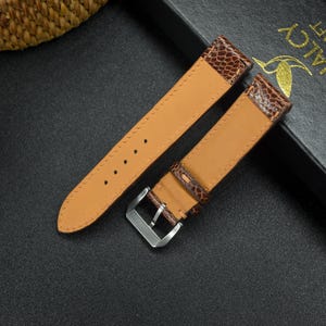 May include: Two brown leather watch straps with a silver buckle. One strap has a textured pattern and the other is smooth.