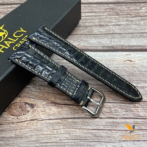 Könnte beinhalten: Schwarzes Lederarmband mit hellbraunen Nähten. Das Armband ist aus echtem Alligatorleder und hat eine silberne Schließe.