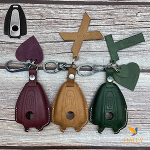 May include: Three leather keychains with different colored key covers. The key covers are burgundy, brown, and green. Each keychain has a different charm attached to it. The charms are a heart with the word "Shelby" on it, a cross with the word "Xavi" on it, and a rectangle with the word "Torres" on it.