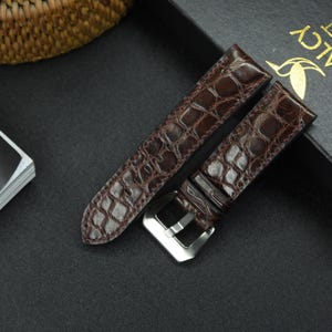 May include: Two brown leather watch straps with a crocodile pattern. One strap has a silver buckle.