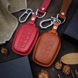 Puede incluir: Dos fundas de cuero para llaves con llaveros. Una es roja y la otra es marrón. Ambas tienen cuatro botones en la parte delantera.