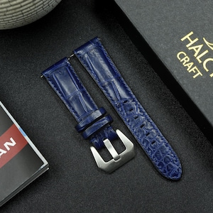 May include: Two navy blue watch straps with a crocodile pattern. The straps have a silver-colored buckle and are displayed on a dark surface. The straps are new and unused.