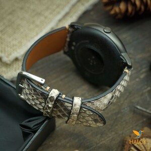 Pode incluir: Um smartwatch preto e prata com uma pulseira de pele de cobra branca e marrom.