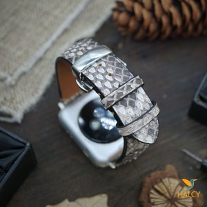 May include: A white and gray snakeskin watch band with a silver buckle. The band is made of genuine leather and is designed for Apple Watches.