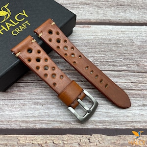 Könnte beinhalten: Zwei braune Lederarmbänder mit perforiertem Design und cremefarbener Naht. Die Armbänder befinden sich auf einer schwarzen Box mit dem Text "HALCY CRAFT" auf der Oberseite.