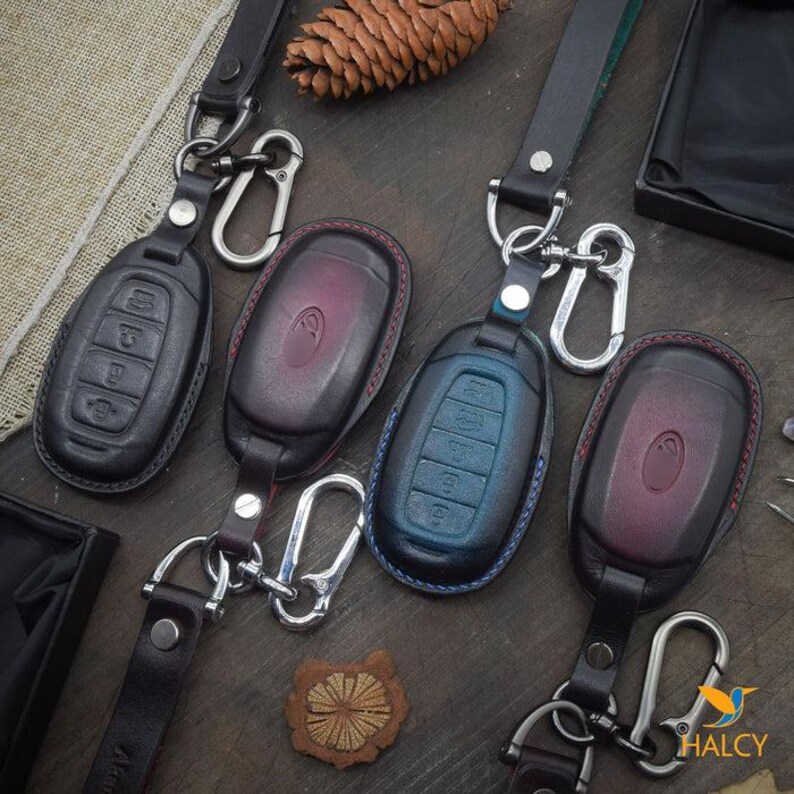 May include: Four leather keychains with different colored key fobs. The key fobs are blue, red, black, and purple. Each keychain has a silver metal ring and a silver metal hook.
