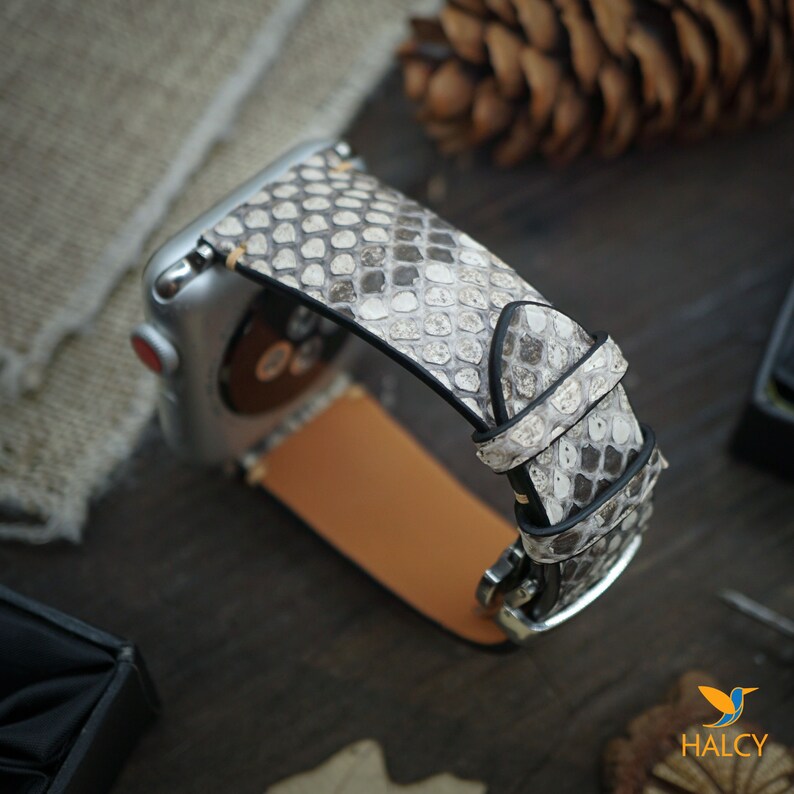 May include: A gray and white snakeskin Apple Watch band with a silver buckle.