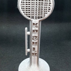 May include: A silver 3D printed model of a microphone with a circular grill and a stand.