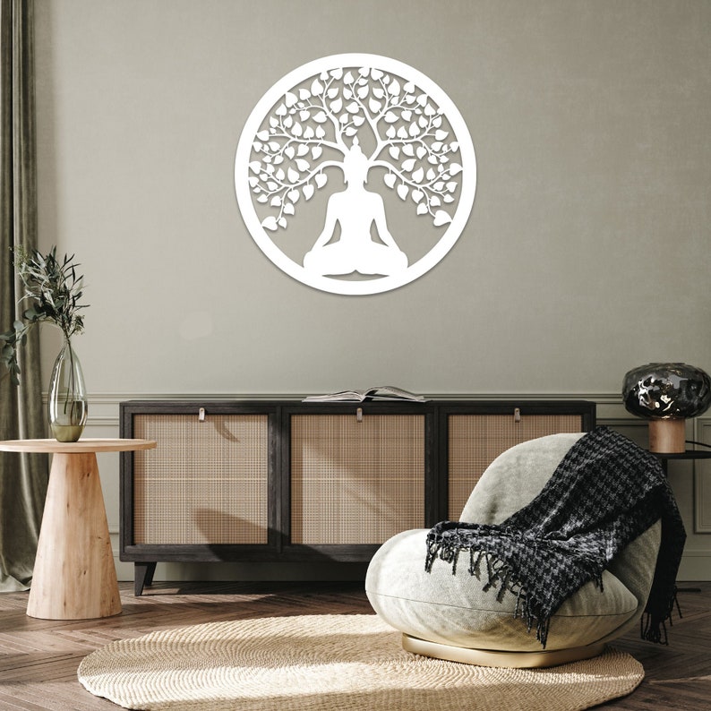 May include: A white, circular wall art piece featuring a meditating figure beneath a tree. The design is cut out, creating a silhouette effect. The artwork is mounted on a neutral-colored wall, adding a touch of serenity to the space.