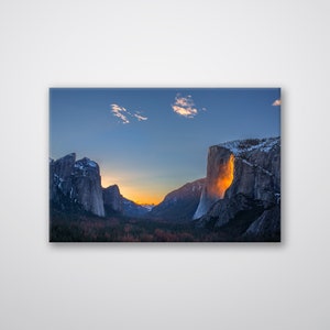 May include: A canvas print featuring a scenic landscape of a mountain valley at sunset. The image captures the golden light illuminating a waterfall and the surrounding cliffs, with a blue sky and clouds above.