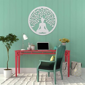 May include: A round, silver-colored metal wall art piece depicting a meditating figure under a tree. The artwork is mounted on a light green wall above a red desk. A laptop, lamp, and chair are also visible.