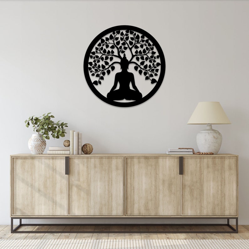 May include: A black metal wall art piece featuring a meditating Buddha figure under a tree, enclosed within a circular frame. The design is a silhouette, with intricate details of leaves and branches. This decorative piece is suitable for meditation spaces or home decor.