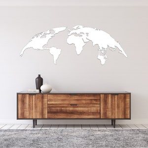 May include: A white, stylized world map wall decor is mounted on a white wall above a wooden cabinet. The cabinet has a dark top, two drawers, and two doors. Decorative vases and books are on the cabinet.