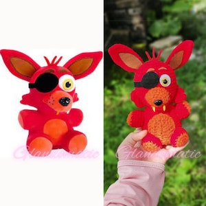 Puede incluir: Juguete de peluche de zorro rojo con un parche en el ojo, una sonrisa de dientes y detalles naranjas. El juguete est&aacute; sentado sobre una superficie blanca.