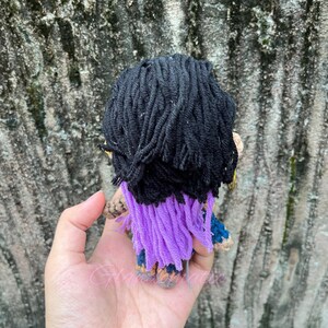 K&ouml;nnte beinhalten: Eine geh&auml;kelte Puppe mit schwarzen Haaren, lila und blauen Kleidern und einem goldenen Schl&uuml;sselanh&auml;nger.