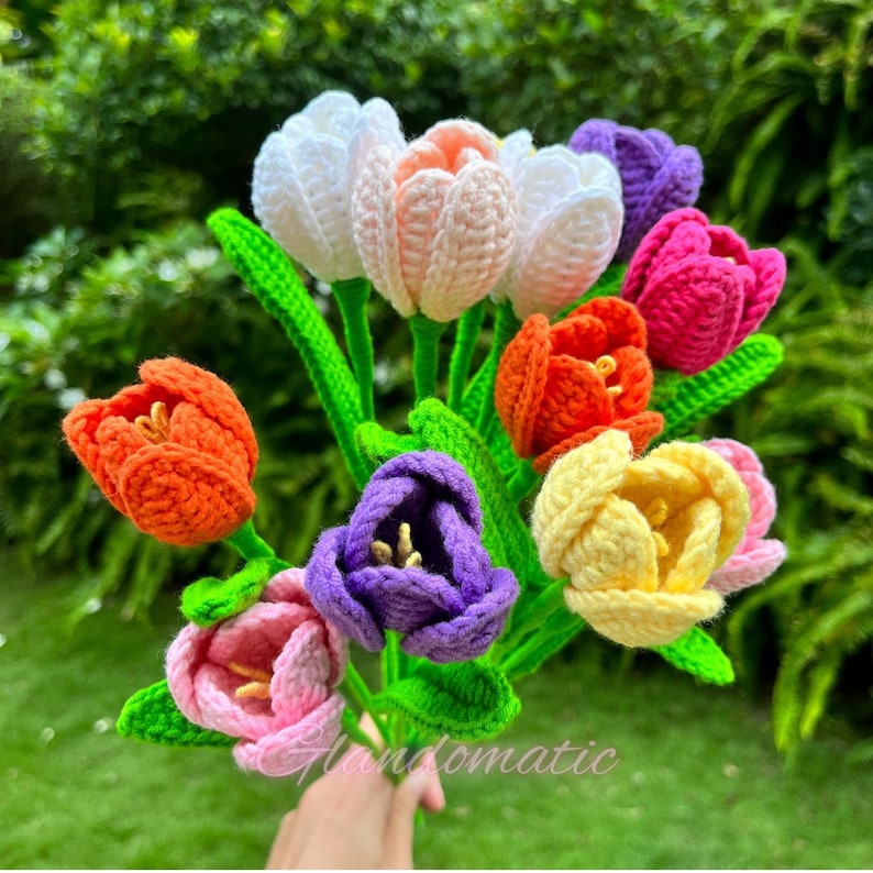 May include: A bouquet of handmade crochet tulips in various colors, including white, pink, orange, purple, and yellow. The flowers have green stems and leaves. The text "Glandomatic" is visible in the bottom right corner.