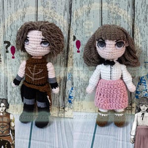 Op de afbeelding: Twee handgemaakte gehaakte poppen. De ene pop heeft bruin haar, een bruin vest, een zwarte broek en grijze accenten. De andere pop heeft bruin haar, een wit shirt, een roze rok en een zwarte strik. Beide poppen hebben grote ogen.