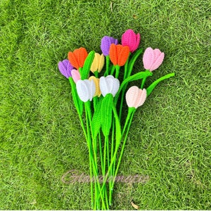 May include: A bouquet of handmade crochet tulips in various colors, including orange, purple, pink, white, and yellow. The flowers have green stems and leaves, arranged against a backdrop of green grass.
