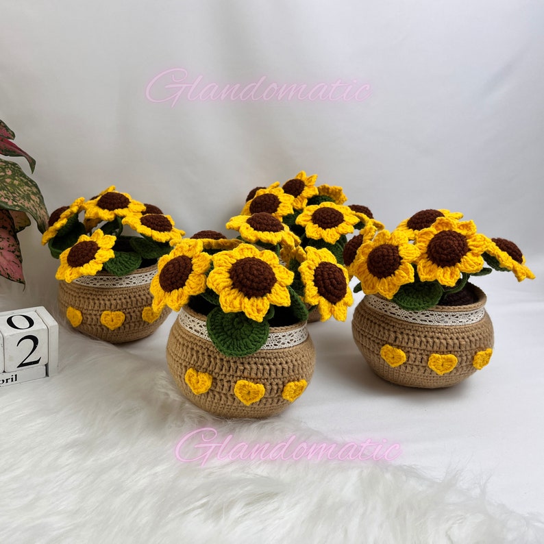 Peut inclure: Trois arrangements de tournesols en crochet dans des pots marrons avec des c&oelig;urs jaunes. Chaque pot est orn&eacute; d'une bordure en crochet blanc. Les tournesols sont jaunes avec des centres marrons.