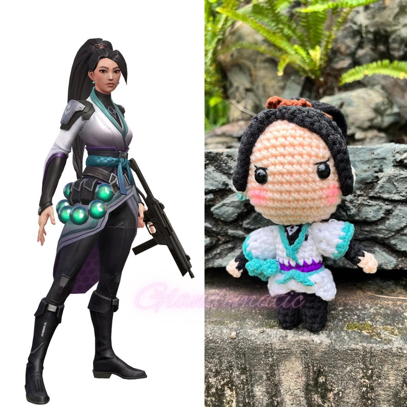 Pu&ograve; includere: Una bambola amigurumi all'uncinetto di un personaggio femminile con capelli neri, un vestito bianco e turchese e una fascia viola. La bambola ha occhi grandi e un'espressione carina. La bambola &egrave; seduta su una roccia con piante verdi sullo sfondo.