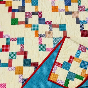 May include: A patchwork quilt with a cream background and a variety of colorful squares in different patterns. The quilt is folded in half, revealing a blue backing with a white polka dot pattern.