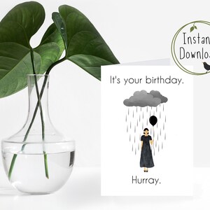 May include: A birthday card with a black and white illustration of a person holding a black balloon under a gray rain cloud. The text on the card reads "It's your birthday. Hurray."