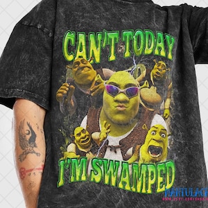May include: Black t-shirt featuring a graphic of Shrek wearing sunglasses, surrounded by other Shrek characters. The text "CAN'T TODAY I'M SWAMPED" is printed in green and yellow. The shirt has a vintage, washed look.