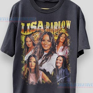 May include: Charcoal grey t-shirt with a retro graphic of Lisa Barlow and the text "LISA BARLOW" in gold. The design incorporates several images of Lisa Barlow. The t-shirt is displayed on a wooden hanger.