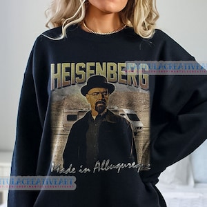 Puede incluir: Sudadera negra con un estampado gráfico de un hombre con sombrero y gafas de sol. El texto "Heisenberg" está impreso encima de la imagen y "Made in Albuquerque" está impreso debajo de la imagen.