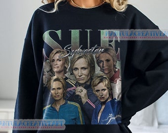 May include: Black crew neck sweatshirt with a vintage-style design featuring the name "Sylvester" and the word "SUE". The design is a collage of images of a person in different outfits. The sweatshirt is a dark colour.