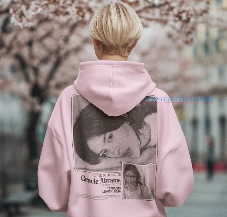 May include: A pink hoodie with a black and white photo of a woman on the back. The photo has the text "GOOD RIDDANCE Gracie Abrams February 24, 2023 12 TRACKS LENGTH: 52:24" printed below it.
