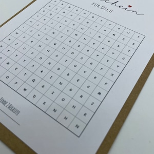 May include: A white card with the word "Gutschein" written in cursive, followed by the words "F&Uuml;R DICH" in all caps. Below the text is a grid of letters, with the instructions "FINDE 2 BEGRIFFE" at the bottom.