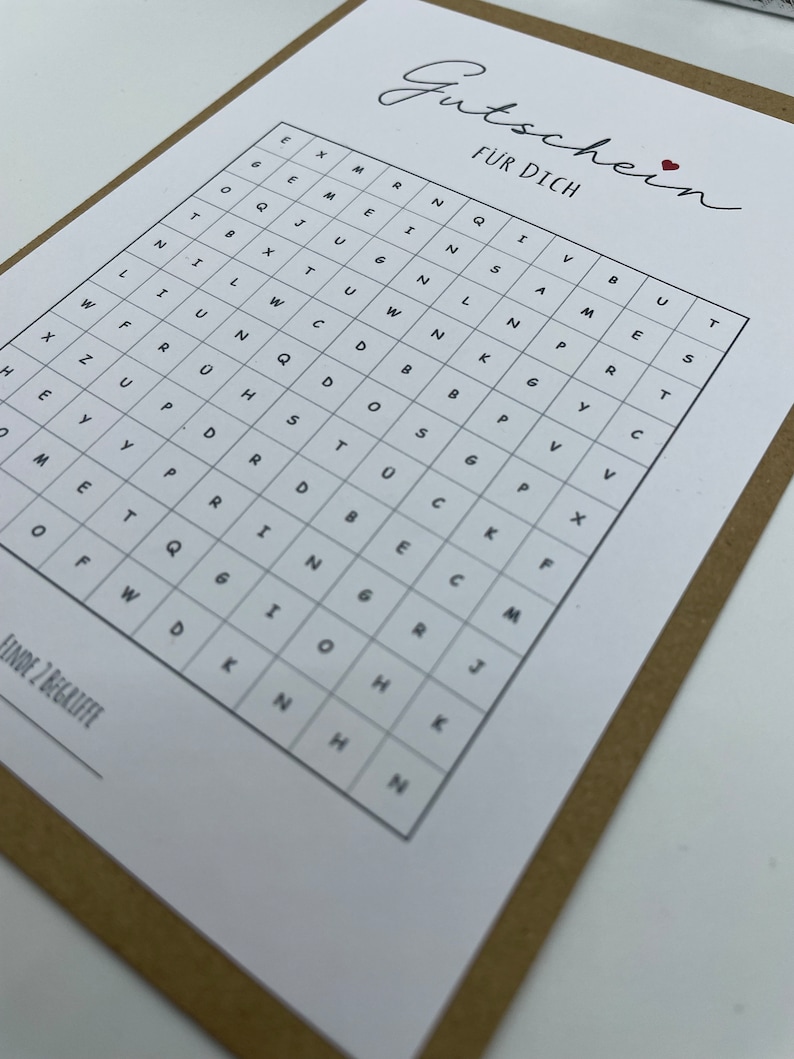 May include: A white card with the word "Gutschein" written in cursive, followed by the words "F&Uuml;R DICH" in all caps. Below the text is a grid of letters, with the instructions "FINDE 2 BEGRIFFE" at the bottom.