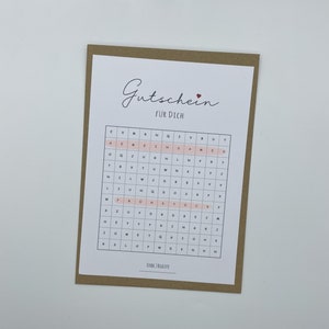 May include: A brown card with the text "Gutschein f&uuml;r Dich" (Gift certificate for you) and a pink grid with letters. The grid has the words "FINDE 2 BEGRIFFE" (Find 2 terms) at the bottom.