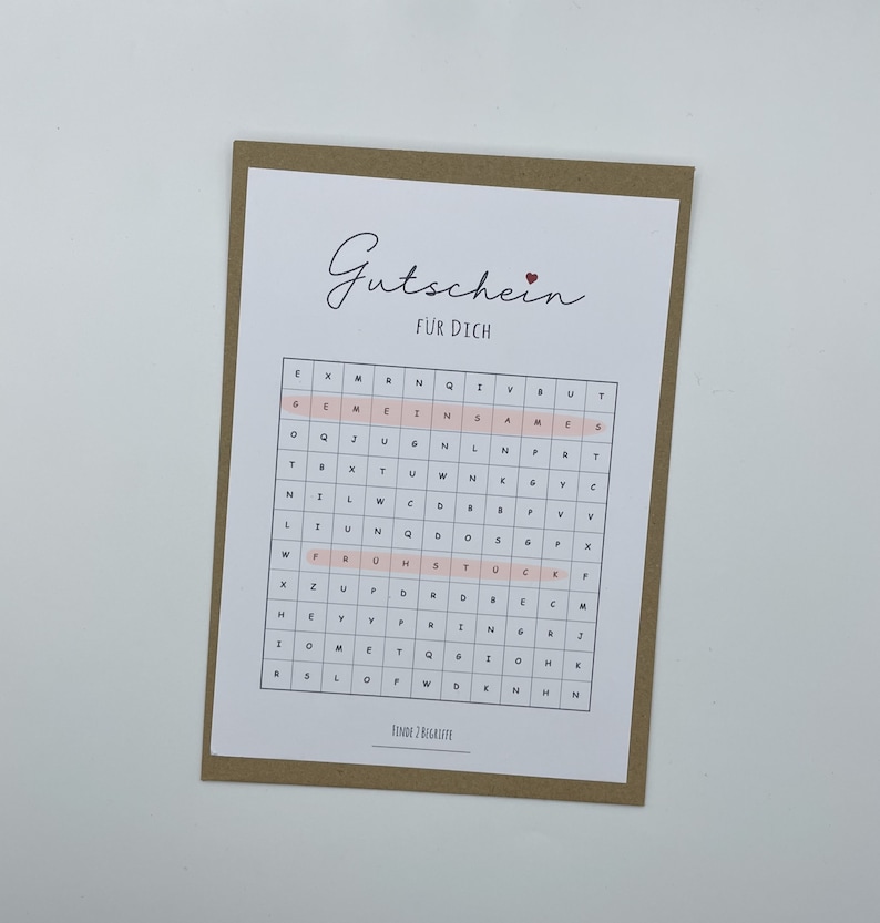 May include: A brown card with the text "Gutschein f&uuml;r Dich" (Gift certificate for you) and a pink grid with letters. The grid has the words "FINDE 2 BEGRIFFE" (Find 2 terms) at the bottom.