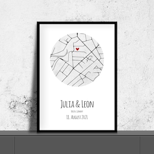 Könnte beinhalten: Schwarz gerahmter Druck mit einer kreisförmigen Karte von Berlin, Deutschland, markiert mit einem roten Herz. Die Namen "JULIA & LEON" und das Datum "18. AUGUST 2021" sind darunter. Der Druck ist vor einer weißen Wand ausgestellt.