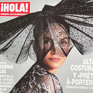Peut inclure: Couverture du magazine ¡HOLA! avec une femme portant un chapeau noir orné et un haut transparent. Le titre du magazine est en rouge et blanc. Le texte comprend "ALTA COSTURA" et "PRIMAVERA-VERANO 2024".