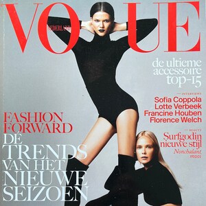 Puede incluir: Portada de la revista Vogue Países Bajos con dos modelos. La modelo de la izquierda lleva un mono negro de cuello alto y botas negras. La modelo de la derecha lleva pantalones de cuero negro con cordones y un top corto negro. El texto de la portada de la revista dice "Fashion Forward" y "De Trends Van Het Nieuwe Seizoen".