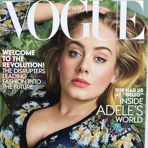 Peut inclure: Une couverture de magazine mettant en scène Adele, une chanteuse, portant un haut noir à paillettes. La couverture est pour le magazine Vogue, numéro de mars, et présente le texte "Bienvenue dans la révolution ! Les perturbateurs qui mènent la mode vers l'avenir" et "Le changement extraordinaire du printemps".