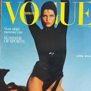 Puede incluir: Portada de la revista Vogue Nederland. Una persona con un body negro con capucha y brazos levantados. La portada incluye el texto: "Voor altijd nummer één", "SUMMER OF SPORTS", y "STRONGER FASTER HARDER". La modelo tiene pintalabios naranja y una banda amarilla en la pierna.