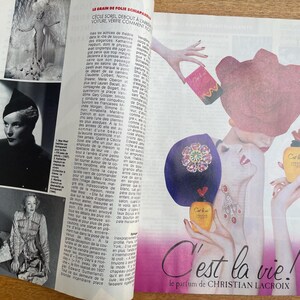 May include: A magazine page featuring a perfume advertisement. The ad showcases an illustration of a woman with a large pink hat and a bottle of perfume. The text "C'est la vie!" is prominently displayed, along with the brand name.