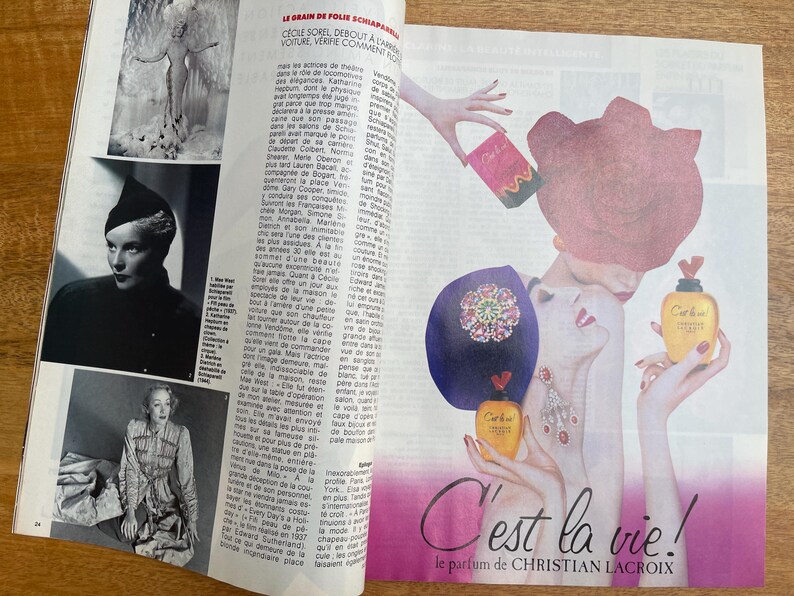 May include: A magazine page featuring a perfume advertisement. The ad showcases an illustration of a woman with a large pink hat and a bottle of perfume. The text "C'est la vie!" is prominently displayed, along with the brand name.