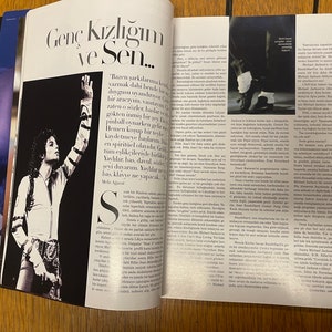 May include: A black and white photograph of a young man singing on stage. He is wearing a white jacket with black stripes and black trousers. The text "Gen&ccedil; Kızlığım ve Sen..." is printed in large white letters on the page. The text "Bazen şarkılarıma kendi duygumu dahil  bensede bir  day gus u  yandirıyor.  " is printed in smaller white letters on the page.
