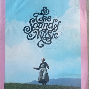 Può includere: Un poster vintage di "The Sound of Music" presenta una donna in un campo con le braccia tese, sullo sfondo di un cielo blu nuvoloso. Il titolo è in una scrittura decorativa. Il poster ha un bordo rosa.