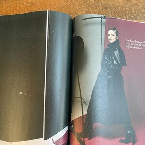 May include: A fashion magazine spread featuring a woman in a black leather coat and boots. The background is a deep red. Text in Dutch is visible on the right page.