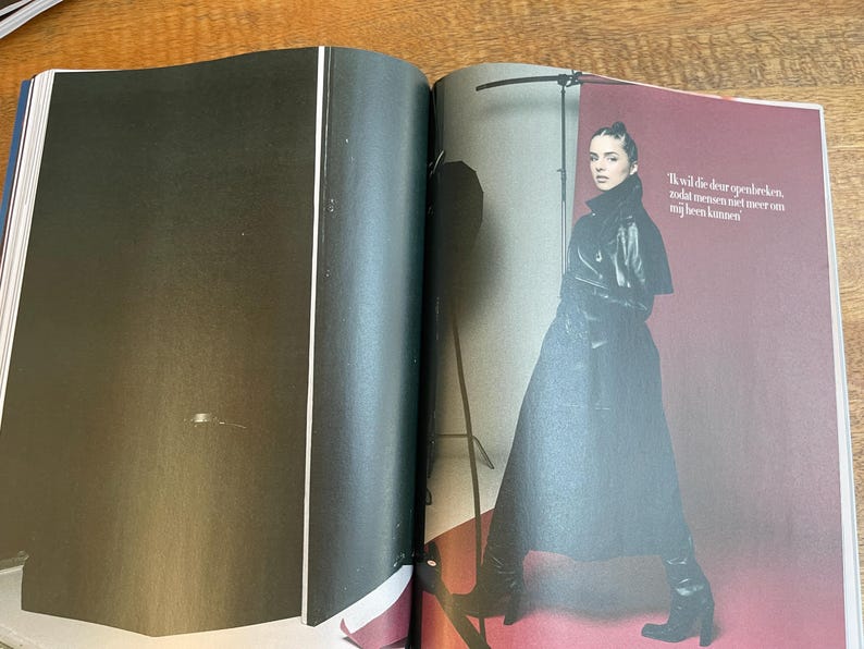 May include: A fashion magazine spread featuring a woman in a black leather coat and boots. The background is a deep red. Text in Dutch is visible on the right page.