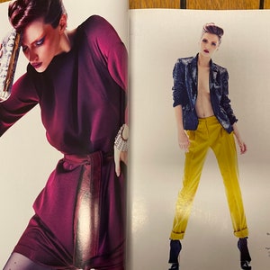 May include: Two women modelling fashion. The woman on the left is wearing a burgundy dress with a gold belt and a silver clutch. The woman on the right is wearing a black sequined jacket, yellow trousers, and black heels.