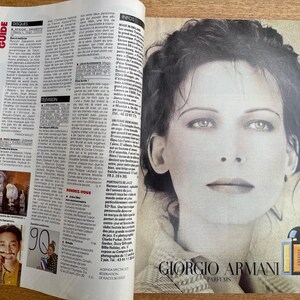 May include: A magazine spread featuring a black and white portrait of a woman and text. The right page displays a close-up of a woman's face, with the Giorgio Armani Parfums logo at the bottom. The left page contains columns of text and images.