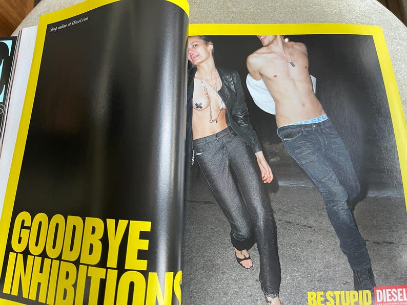 May include: A magazine spread featuring two models in Diesel clothing. The woman wears a black leather jacket and dark denim pants. The man wears jeans and has a white shirt draped over his shoulders. The text "GOODBYE INHIBITIONS" is visible.