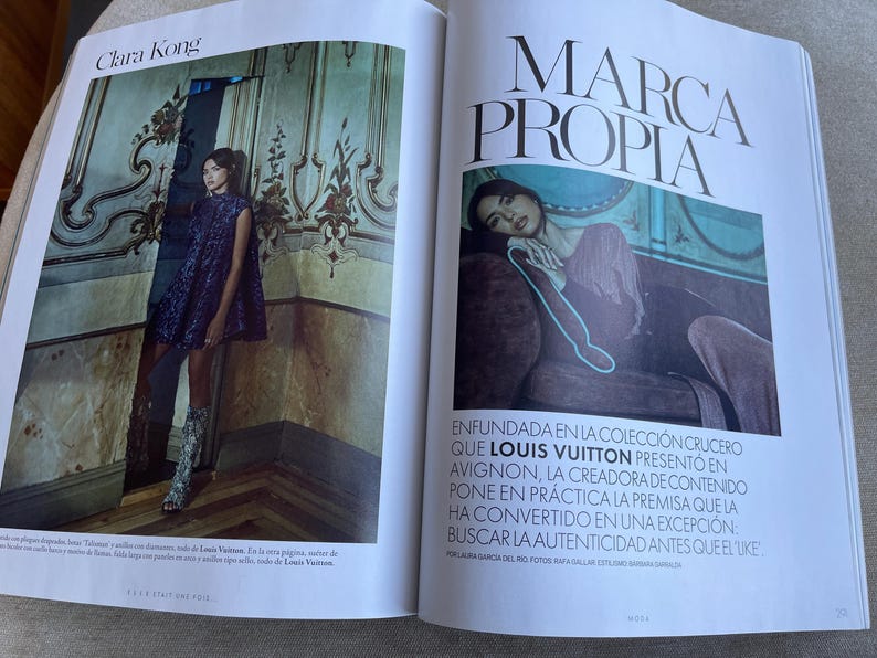 Puede incluir: Una revista de moda de doble p&aacute;gina. Una p&aacute;gina presenta a una modelo con un vestido azul oscuro y botas estampadas. La otra p&aacute;gina tiene el texto "MARCA PROPIA". Tambi&eacute;n se ve el nombre "Clara Kong".